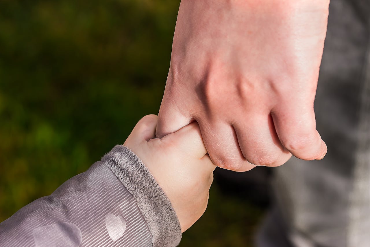 home-hero A close-up of a child and parent holding hands in a park, symbolizing love and trust.